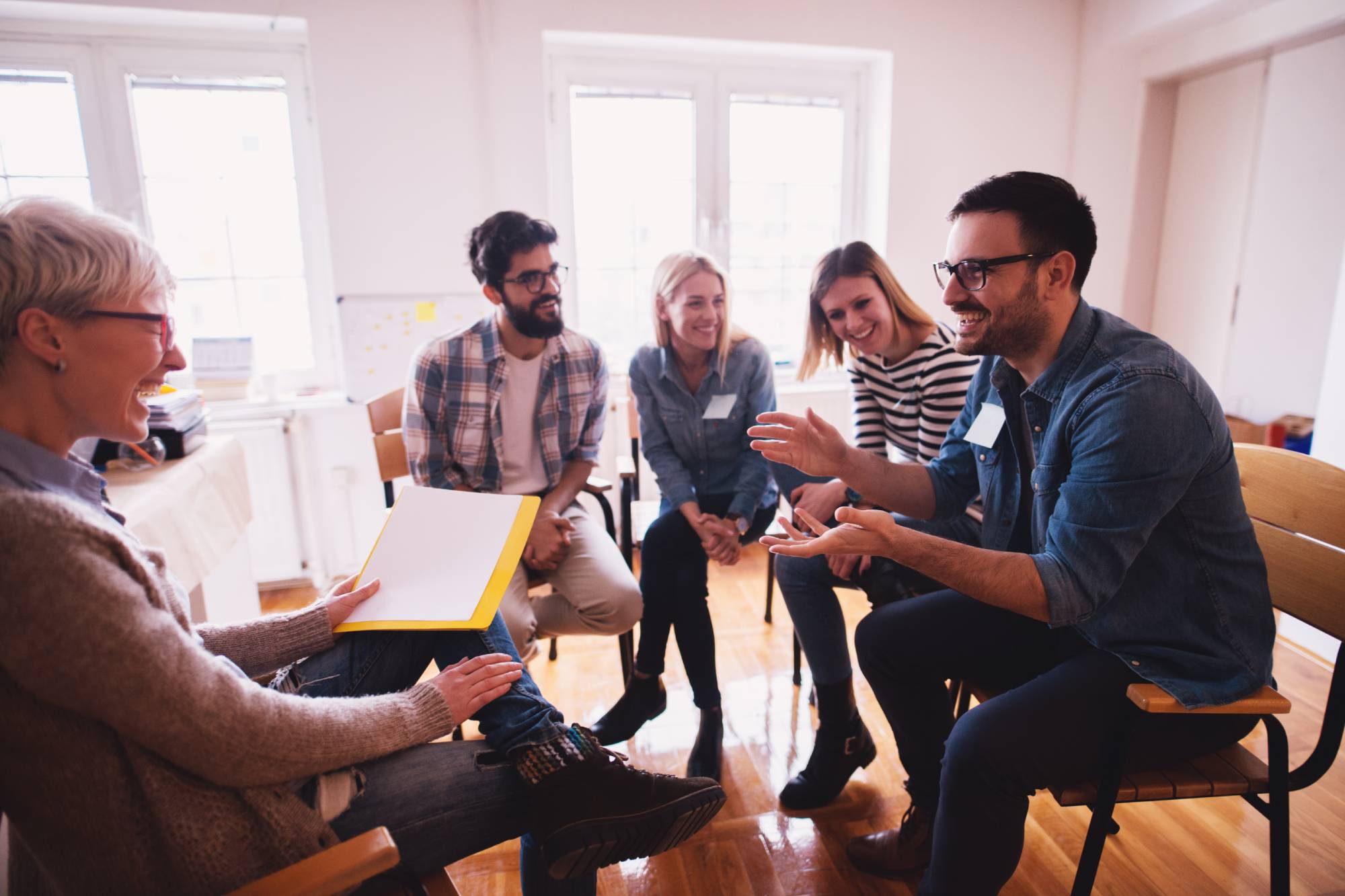 Young addicted people enjoying spending time together on special group therapy. Handsome joyful guy talking jokes and making fun.